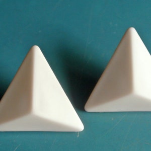 Pode incluir: Duas peças de cerâmica de forma triangular branca. As peças são lisas e têm um acabamento brilhante.