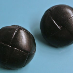 Puede incluir: Dos bolas de cuero negro con un patrón cosido. Las bolas están sobre un fondo azul claro.