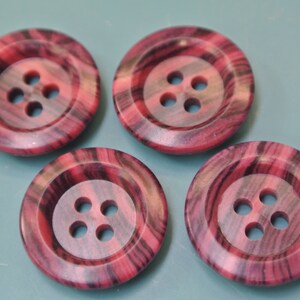 Puede incluir: Cuatro botones rayados de color rosa y negro con cuatro agujeros cada uno.