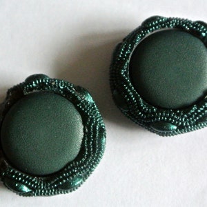 Op de afbeelding: Twee donkergroene knoppen bekleed met stof met een decoratieve parelrand.
