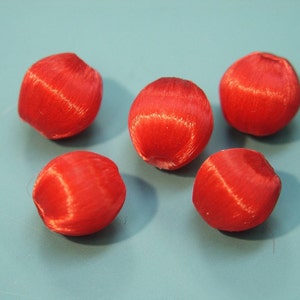 May include: Five red satin covered beads, each with a slightly different shape and texture.