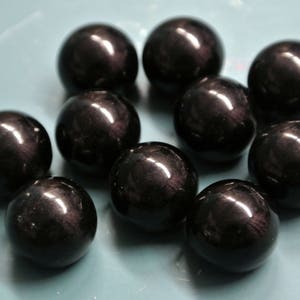 Könnte beinhalten: Zehn schwarze Obsidian-Kugeln mit hochglänzender Oberfläche. Die Kugeln sind glatt und rund.