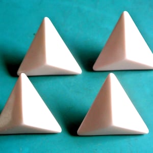 Pode incluir: Quatro objetos em forma de pirâmide, de cor branco-sujo, estão dispostos sobre uma superfície turquesa. Cada pirâmide tem três lados triangulares e uma base plana. Os objetos estão uniformemente espaçados.