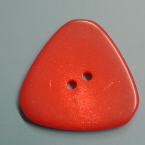 May include: A red triangular button with two holes in the centre. The button has a slightly glittery finish.