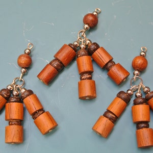 Puede incluir: Varios adornos de cuentas de madera hechos a mano. Cada adorno presenta un grupo de cuentas de madera cilíndricas y redondas en tonos marrones, conectadas por herrajes metálicos plateados. Las cuentas están dispuestas en un patrón ramificado.