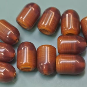 Könnte beinhalten: Eine Sammlung von zehn braunen und violetten Perlen mit glänzender Oberfläche. Die Perlen sind oval geformt und haben eine leichte Größenvariation.