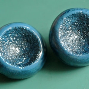 May include: Two blue ceramic ornaments with a textured surface and a metallic sheen.