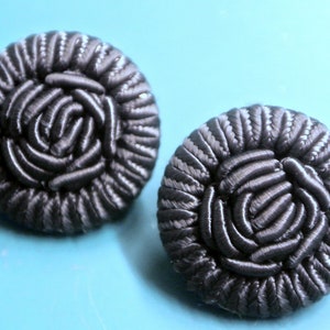 Puede incluir: Un par de pendientes de tela negra con un diseño de roseta.