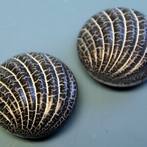 May include: Two round buttons in black and white with a textured, ribbed design. The buttons have a raised, circular pattern.