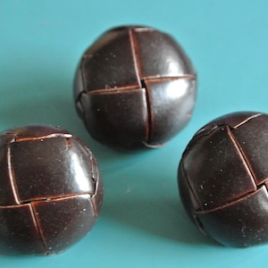 Op de afbeelding: Drie bruine lederen ballen met een gestikt patroon. De ballen zijn in een driehoekige vorm op een blauw oppervlak gerangschikt.