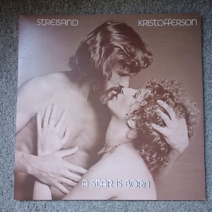 May include: Album cover for "A Star Is Born" featuring Streisand and Kristofferson. The sepia-toned image shows a man and woman embracing, with the man kissing the woman. The album title is displayed at the bottom.