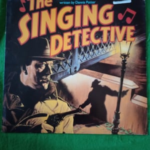 Op de afbeelding: Albumhoes voor "The Singing Detective" met een man met een hoed die een pistool vasthoudt, met een silhouet van een figuur op een brug. De titel staat in grote gele letters met rode accenten en de hoes heeft een vintage esthetiek.