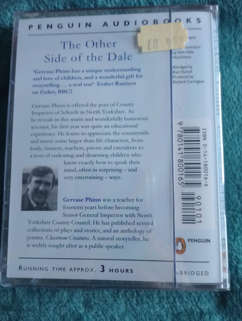 Op de afbeelding: Een Penguin Audiobooks cassette van "The Other Side of the Dale" van Gervase Phinn. De cover bevat tekst en een foto van de auteur. De looptijd is ongeveer 3 uur. De cassette zit in een doorzichtige plastic hoes.