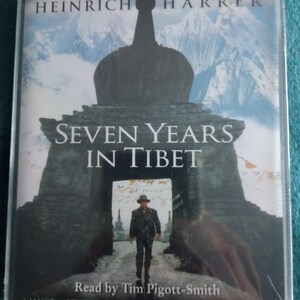 Op de afbeelding: De boekomslag van "Zeven jaar in Tibet" van Heinrich Harrer. Het toont een man die door een boog loopt, met de titel prominent weergegeven. De tekst "Gelezen door Tim Pigott-Smith" is ook zichtbaar.