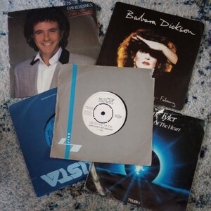 May include: A selection of vinyl record sleeves, featuring album art and artist names. Includes covers for David Essex, Barbara Dickson, and Depeche Mode. The sleeves are in various colours and designs, showcasing different musical artists and album titles.