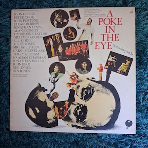 May include: Vintage vinyl record album cover titled "A Poke in the Eye (with a sharp stick)". The cover features a collage of images and text, including the names of the cast members and a skull graphic.