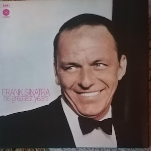 Könnte beinhalten: Ein Schwarzweißfoto von Frank Sinatra auf einem Schallplattencover. Das Cover ist hellblau und trägt den Text "FRANK SINATRA his greatest years" in Pink.