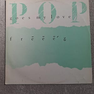 Puede incluir: Una funda de disco de vinilo cuadrada con fondo blanco y una amplia banda horizontal de color verde menta texturizada en el centro. El texto P.O.P goes my love está impreso en verde menta y negro, con el nombre del artista frééé'z en negro.