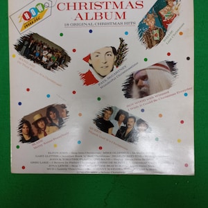 May include: The Christmas Album, featuring 18 original Christmas hits. Album cover includes images of Paul McCartney, Wham, Queen, and Band Aid. The album is on a green surface.