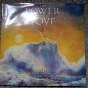 May include: Album cover for "The Power of Love" with a romantic design. The image shows two faces in silhouette kissing, set against a sunset and ocean waves. The title "the POWER of LOVE" is at the top. The text "12 Powerful Love Songs" is below.