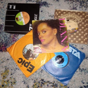 May include: A collection of four 7-inch vinyl records featuring various sleeves. One sleeve displays a portrait of Diana Ross with the text Why Do Fools Fall In Love. Other sleeves include branding from Epic, Casablanca, and Arista record labels.