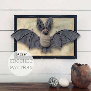 May include: A crochet bat pattern in a black frame with the text "PDF CROCHET PATTERN" in a white circle. The bat is grey and has a brown nose and eyes.