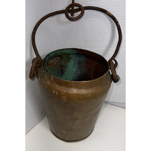 May include: An antique copper bucket with a rusty iron handle. The bucket has a worn, aged patina and is perfect for rustic decor.