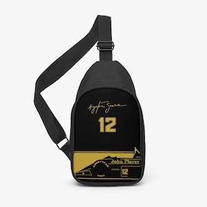 May include: Black sling bag with a gold design. The bag features the name "Ayrton Senna" in a script font, the number "12", and the words "John Player" with a race car graphic. The bag has a black adjustable strap.