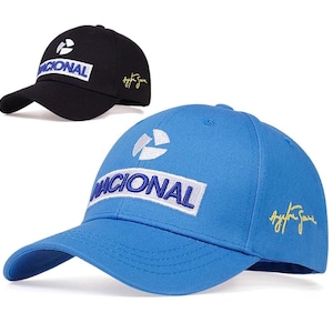 May include: Two baseball caps, one black and one blue, with the word "NACIONAL" embroidered on the front. Both caps have a white logo on the front and a gold signature on the side.