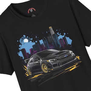May include: Black t-shirt featuring a stylized illustration of a black car with gold wheels, set against a cityscape with a blue and purple sky. The shirt has the text "MOTOR CUSTOM" on the collar.