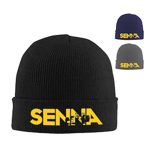 May include: Black knit beanie with a yellow "SENNA" logo. The logo is a stylized font with a distressed look.