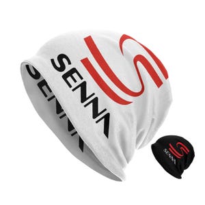 May include: White beanie with a red and black Senna logo. The beanie is folded and shows the inside of the beanie, which is black with a red Senna logo.