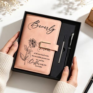 May include: A light peach-colored journal in a black gift box with a matching black pen and refill. The journal cover features a black floral illustration, the name Beverly, and the text: Proud of all your hard work, the incredible person you are, and the difference you make.