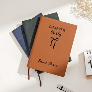 Puede incluir: Una taza de cerámica blanca con asa negra y el texto "But First, Coffee" en negrita negra. La taza se encuentra sobre un fondo borroso, sugiriendo un ambiente acogedor.