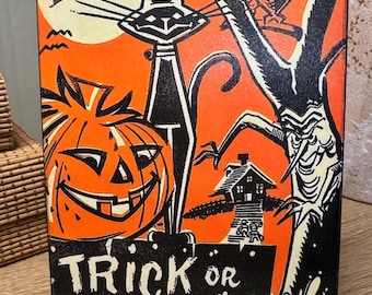 May include: Vintage-style Halloween sign with a black cat, jack-o'-lantern, owl, and witch on a broomstick against an orange background. The sign reads "Trick or Treat" in white text on a black base. A spooky, decorative item.