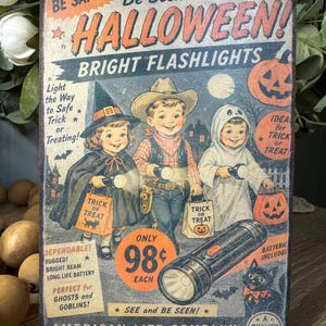 May include: Vintage Halloween-themed sign featuring children in costumes holding flashlights. The sign promotes "Bright Flashlights" with text like "Be Safe!" and "Trick or Treat." Includes a black cat, pumpkins, and the price of 98¢.