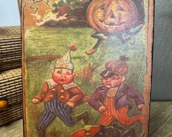 May include: Rectangular Halloween-themed wooden sign with a vintage illustration. The artwork depicts a pumpkin figure and three small figures running across a green field. The word "Halloween" is at the top in an ornate font. The sign has a distressed, aged appearance.