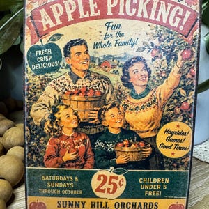 May include: Vintage-style wooden sign advertising apple picking at Sunny Hill Orchards. The sign features a family picking apples, with text that reads "Join Us For Apple Picking!" and "Fun for the Whole Family!" Includes "Fresh Crisp Delicious!" and "Hayrides! Games! Good Times!"