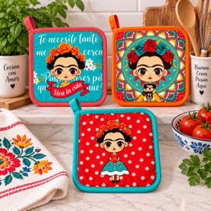 May include: Three square pot holders featuring a cartoon-style Frida Kahlo illustration. One is teal with Spanish text and a red banner, one is orange with a mandala pattern, and one is red with a white floral print and a full-body character design.