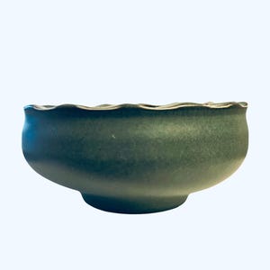 May include: A dark green ceramic bowl with a wavy rim. The bowl has a rounded shape and a small, circular base. The rim has a lighter, contrasting color. The bowl is likely used for serving food or as a decorative item.