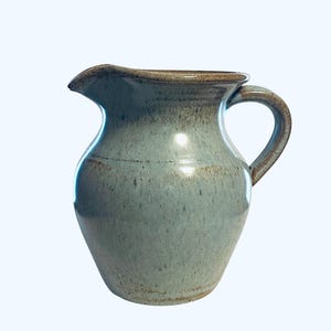 May include: A white ceramic mug with a black handle and the text "But First, Coffee" in a bold, black font. The mug is set against a blurred background, suggesting a cozy setting.