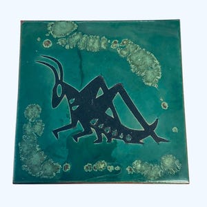 May include: A green ceramic tile with a black silhouette of a grasshopper. The tile has a speckled green glaze.