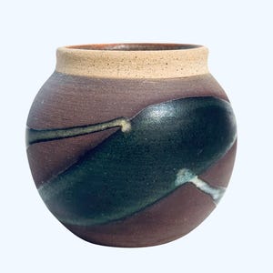 May include: A handcrafted ceramic vase with a rounded body and a wide opening. The vase features a dark brown base color with a large, dark green abstract design. The rim is a light tan color.