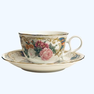 May include: A white teacup and saucer set with a floral design. The teacup and saucer are decorated with pink, orange, and white flowers, with gold trim. The handle of the teacup is curved.