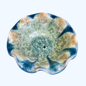 May include: A decorative ceramic bowl with a unique, organic design. The bowl features a scalloped edge and a color palette of teal, blue, and beige. The interior has a textured, crystalline pattern, while the rim is a deep blue.