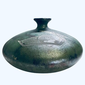 May include: A handcrafted, oval-shaped ceramic vase with a dark green, textured finish. The vase features a silver-colored etched design on the front. The vase has a small, cylindrical neck and is suitable for home decor.