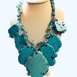 May include: A turquoise statement necklace with large, irregularly shaped pendants. The necklace features a mix of polished and raw turquoise stones, connected by silver-toned metal links and a strand of small turquoise chips.
