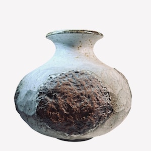 May include: A handcrafted ceramic vase with a bulbous body and a narrow neck. The vase features a textured, earthy brown patch on a light gray and white speckled surface. The rim is a darker shade of gray.