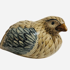 May include: A ceramic bird figurine with brown and black painted details. The bird is sitting on its belly with its head turned to the side. The bird has a brown beak and black eyes.