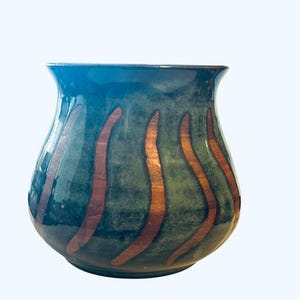 May include: A handcrafted ceramic vase with a rounded body and a flared rim. The vase is primarily teal with vertical copper-colored stripes. The interior and rim are a darker teal. This decorative vase is suitable for home decor.